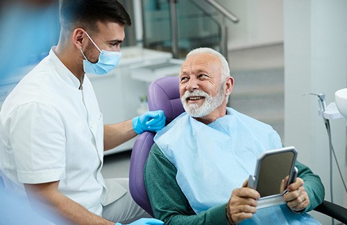 Senior patient looking at dentist while holding small mirror