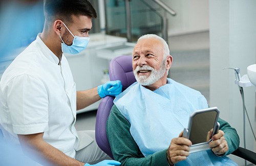 Senior patient looking at dentist while holding small mirror