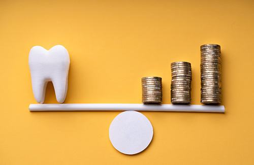 a scale balancing a model tooth and coins