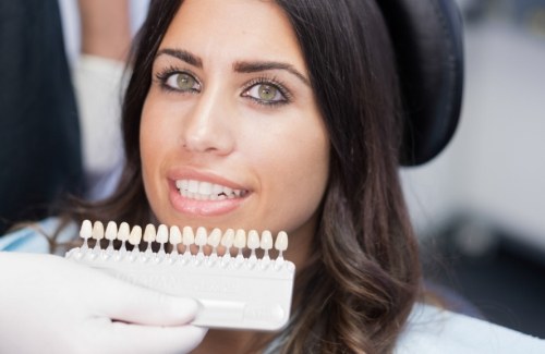 Woman in dental chair smiling while dentist holds shade guide