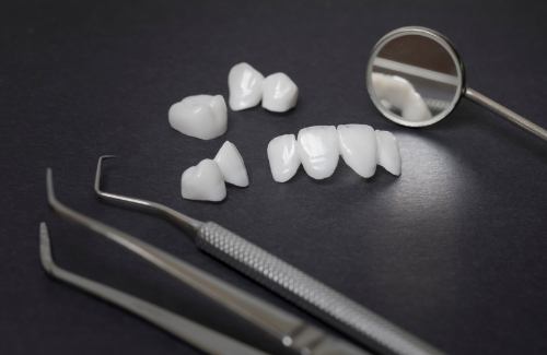 Several white dental crowns and veneers on table next to dental instruments