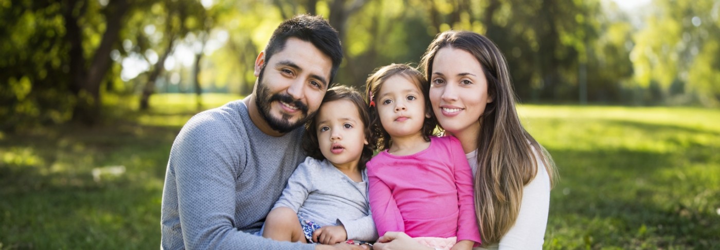 Smiling family of four sitting in grass after receiving dental services in West Jordan