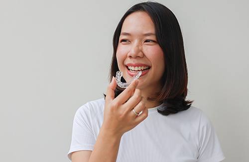Woman smiling while holding clear aligner