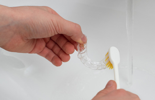 Patient using toothbrush to clean aligner