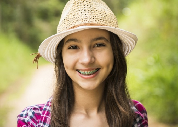 Teenage girl with braces smiling outdoors in straw hat