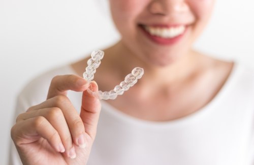 Smiling person holding an Invisalign clear aligner