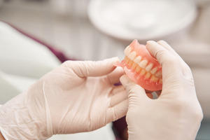 Gloved hands holding full dentures